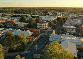 Aerial view of a quiet small town at sunset, with tree-lined streets, low-rise buildings, and a mostly empty parking lot, bathed in warm golden light.