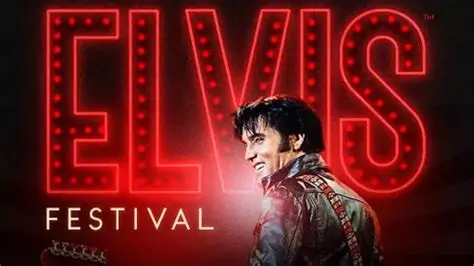 A man in an Elvis costume smiles in front of large neon text reading “ELVIS FESTIVAL” with a guitar strap over his shoulder.